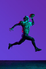 Full-length portrait of male american fotball player training isolated over dark purple studio background