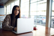© BullRun - Portrait of hipster girl with modern laptop computer looking at camera during remote working in cafe interior, skilled female freelance copywriter with digital netbook technology posing at desktop