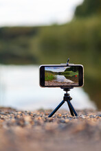 A Close Up Of The Phone On A Tripod Takes A Video Or A Photo Of Nature. A Beautiful Lake In The Forest With Clouds In The Screen Of The Photographer's Mobile Phone. 