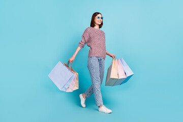 Wall Mural - Profile photo of cute lady walk carry retail bags wear sunglass sweater jeans shoes isolated blue color background