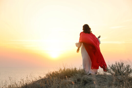 Jesus Christ on hills at sunset, back view. Space for text