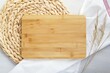 Wooden cutting board mockup, top view composition with wicker mat, kitchen towel and dried plants, kitchen flat lay with chopping board for text or engraving.