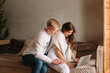 © Елизавета Старкова - A smiling young man and a woman in love are sitting on the sofa hugging working using wireless technologies looking at a laptop and a phone during the winter holidays in a cozy house