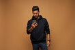 © Тарас Нагирняк - Handsome indian student in black hoody surfing his mobile phone on background