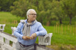 © Studio Romantic - Happy elderly man with a book in his hands is resting in the park outdoors. A retired man stands at the fence in the park, smiling and holding a book.