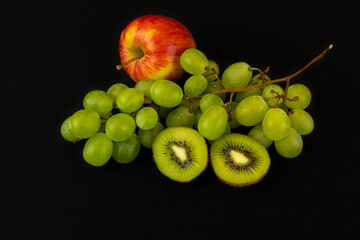 Poster - Closeup shot of fresh slices of kiwis, apple, and green grapes isolated on a dark background