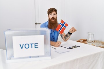 Canvas Print - Caucasian man with long beard at political campaign election holding norwegian flag scared and amazed with open mouth for surprise, disbelief face