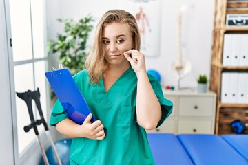 Poster - Young caucasian woman working at pain recovery clinic mouth and lips shut as zip with fingers. secret and silent, taboo talking