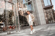 © Marharyta Hanhalo - Attractive serious sad upset young blonde man walks holding skateboard on shoulder at city street among glass buildings.
