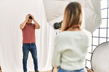 Wall Mural - Woman photographer talking pictures of man posing as model at photography studio suffering from headache desperate and stressed because pain and migraine. hands on head.