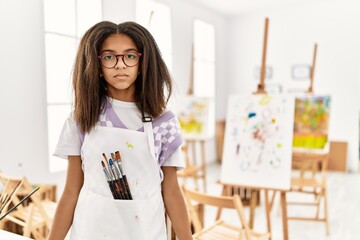 Poster - Young african american girl painting at art studio with serious expression on face. simple and natural looking at the camera.