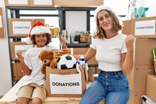 Young Mother With Little Son Wearing Christmas Hat At Donations Stand Screaming Proud, Celebrating Victory And Success Very Excited With Raised Arms