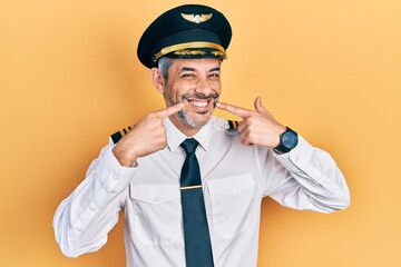 Sticker - Handsome middle age man with grey hair wearing airplane pilot uniform smiling cheerful showing and pointing with fingers teeth and mouth. dental health concept.