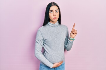 Canvas Print - Beautiful woman with blue eyes expecting a baby, touching pregnant belly pointing up looking sad and upset, indicating direction with fingers, unhappy and depressed.