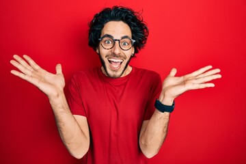 Sticker - Handsome hispanic man wearing casual t shirt and glasses celebrating crazy and amazed for success with arms raised and open eyes screaming excited. winner concept