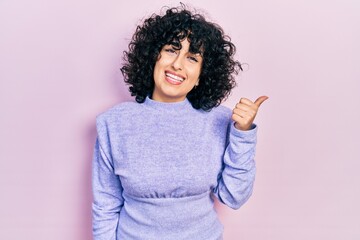 Sticker - Young middle east woman wearing casual clothes smiling with happy face looking and pointing to the side with thumb up.