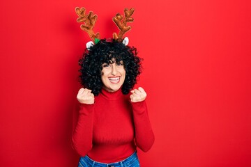 Poster - Young middle east woman wearing cute christmas reindeer horns celebrating surprised and amazed for success with arms raised and open eyes. winner concept.