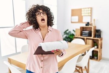 Poster - Young middle eastern woman wearing business style at office crazy and scared with hands on head, afraid and surprised of shock with open mouth