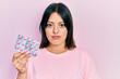 © Krakenimages.com - Young hispanic woman holding pills thinking attitude and sober expression looking self confident