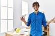 © Krakenimages.com - Young hispanic man using drone at architect office celebrating achievement with happy smile and winner expression with raised hand