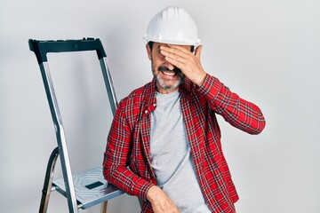 Sticker - Middle age hispanic worker man using ladder stressed and frustrated with hand on head, surprised and angry face