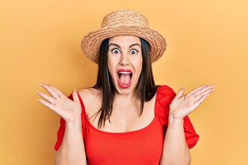 Poster - Young hispanic woman wearing summer hat celebrating crazy and amazed for success with arms raised and open eyes screaming excited. winner concept