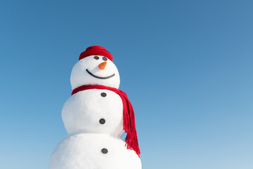 Wall Mural - Funny snowman in stylish red hat and red scalf on snowy field. Blue sky on background