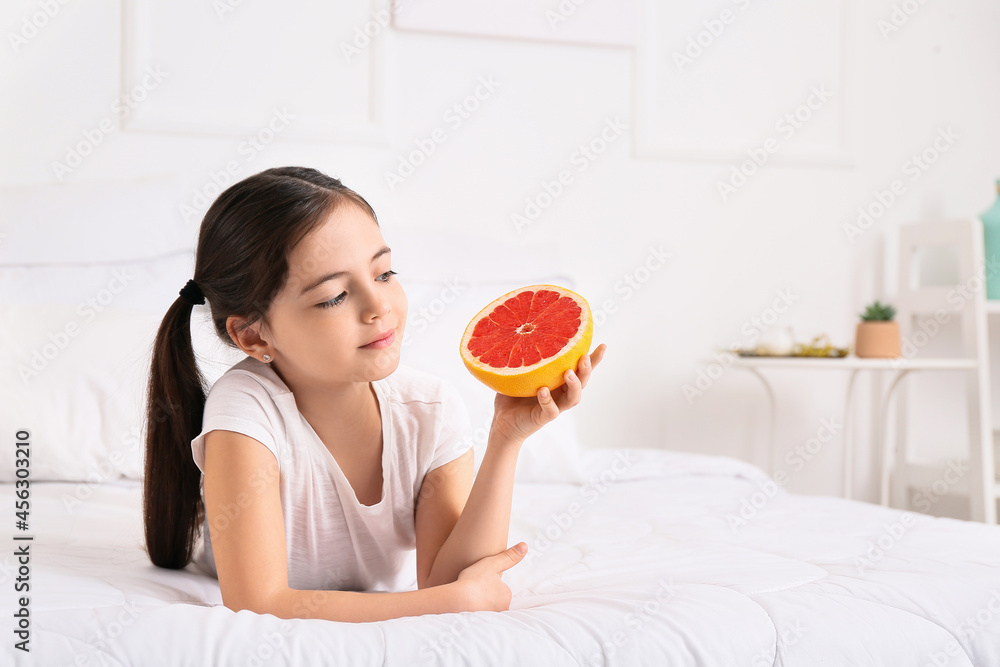 Little girl with fresh tasty grapefruit in bedroom