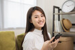 © Chanakon - Happy young asian woman looking at screen of smartphone sitting on sofa in living room she shopping online. She very happy. Teenage girl reading news from mobile phone feeling excited.