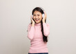 © Chanakon - Cheerful asian female teenager listen to the music with white headphone on isolated. Beautiful young woman in pink shirt hand touch a wireless headphone having fun with the music in  room.