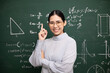 © Chanakon - Young asian teacher woman teaching standing showing index finger and video conference with student looking camera. Female teacher training the mathematics in classroom blackboard from online course.
