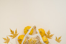Yellow Round Small Pumpkins In An Eco Friendly Mesh Bag And Fallen Maple Leaves On A Light Background. Autumn Composition Flat Lay. Harvesting. Copy Space