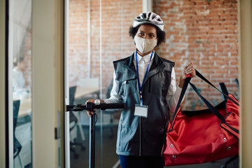 African American food deliverer uses electric push scooter while making delivery during coronavirus pandemic.