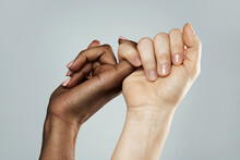 A Pinky Promise Gesture Between African And Caucasian Women. Closeup Of Palms On Gray Background.