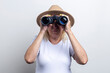 © Alex - Old woman in a hat looking through binoculars on a light background.