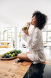 © Daniel - Young african american woman drinking green juice with reusable bamboo straw on kitchen counter. Vertical.