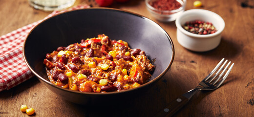 Wall Mural - Chili Con Carne with ground beef, beans and corn in dark bowl on wooden background. Mexican and Texas cuisine