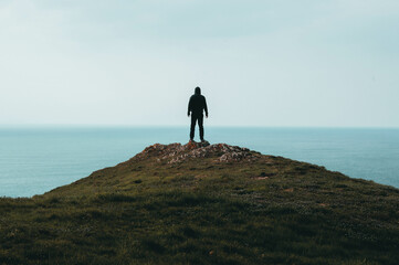 Wall Mural - A lone hooded figure standing on top of a hill, looking out across the ocean.
