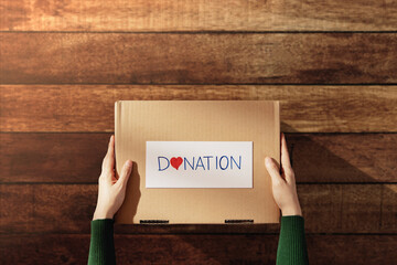 Wall Mural - Donation Concept. Woman with Box of Things with Donate label and Heart. Preparing on Wooden Table at Home. Top View