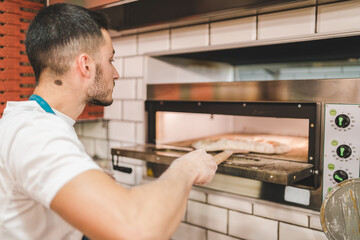 Wall Mural - Closeup shot of a male cook taking out of a stove a delicious pizza