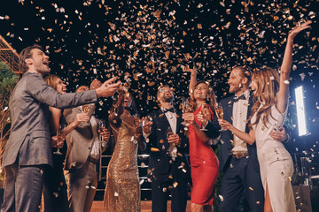 Wall Mural - Group of beautiful people in formalwear having fun together with confetti flying all around