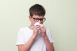 Portrait of a teenage boy blowing his nose in a paper handkerchief.