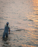 Fototapeta Do akwarium - Unidentified Asian fisher man with waterproof wader and hat throwing a cast net at sunrise