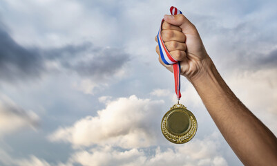 Wall Mural - Medal gold in winner hand. First place award, sky background. Sport champion athlete victory concept