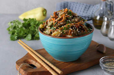 Korean style eggplant salad with sesame seeds, onions and carrots in a blue bowl on a gray background.