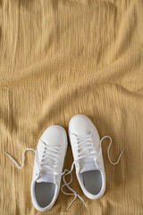 Wall Mural - Fashion blog or magazine concept. White female sneakers on yellow crumpled muslin cloth background. Flat lay, top view minimal background