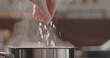 man adding salt to boiling water in saucepan