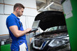 © My Ocean studio - Young confident handsome car mechanic with laptop in hand conducts computer diagnostics for errors in the car systems