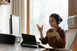 © fizkes - Social distance in office work. Young indian female team leader in earphones meet staff online provide virtual training speak using touchpad webcam. Mixed race business lady talk on internet briefing