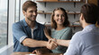 © fizkes - Happy millennial Caucasian man and woman shake hand close deal with male relator or broker at meeting. Smiling couple buyer clients handshake real estate agent make agreement buy home together.
